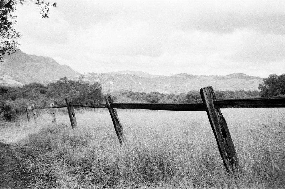 A black and white photo of a fence in a field.