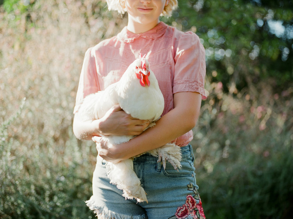 A girl holding a chicken in a field.