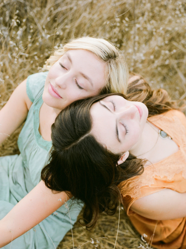Two women laying in a field with their eyes closed.