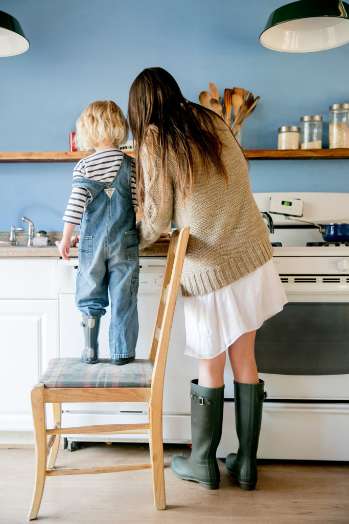 child standing on chair helping mother cook in kitchen