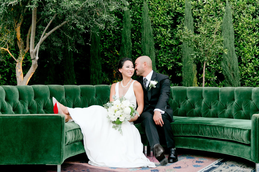 A bride and groom sitting on a green couch.