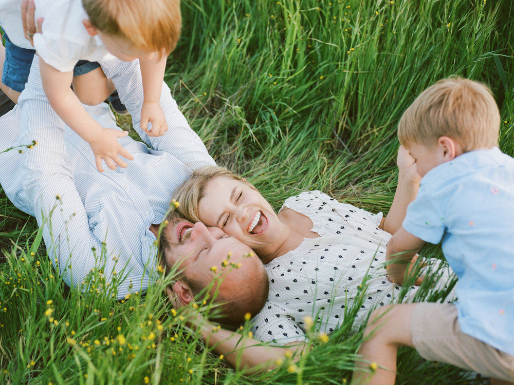 mother laughing while laying in the grass with husband and two young boys