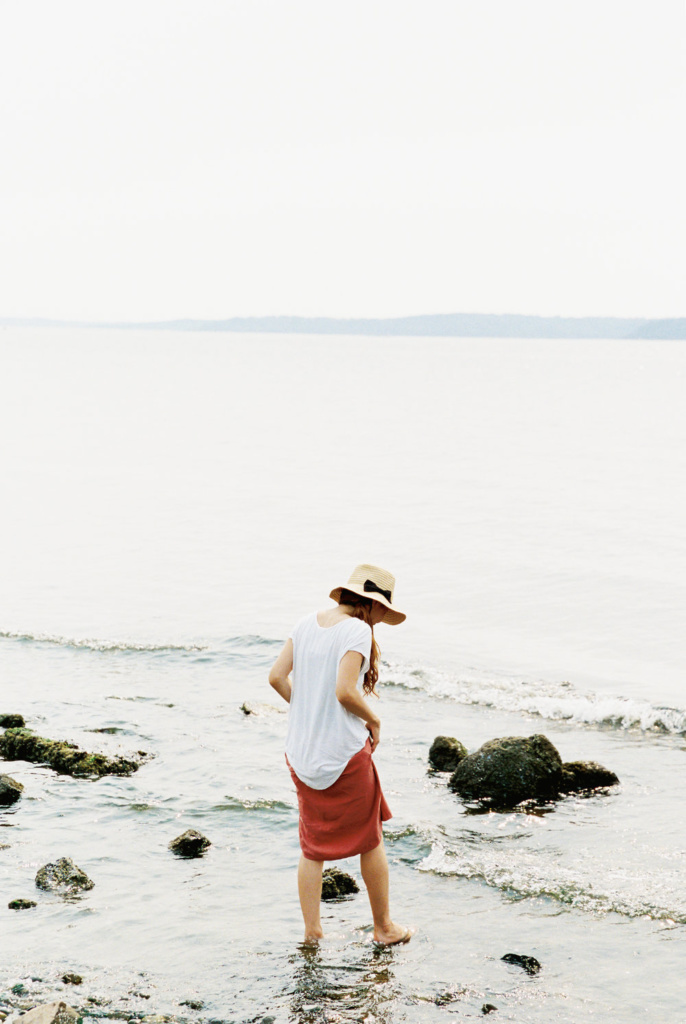 A woman standing in the water with a straw hat.