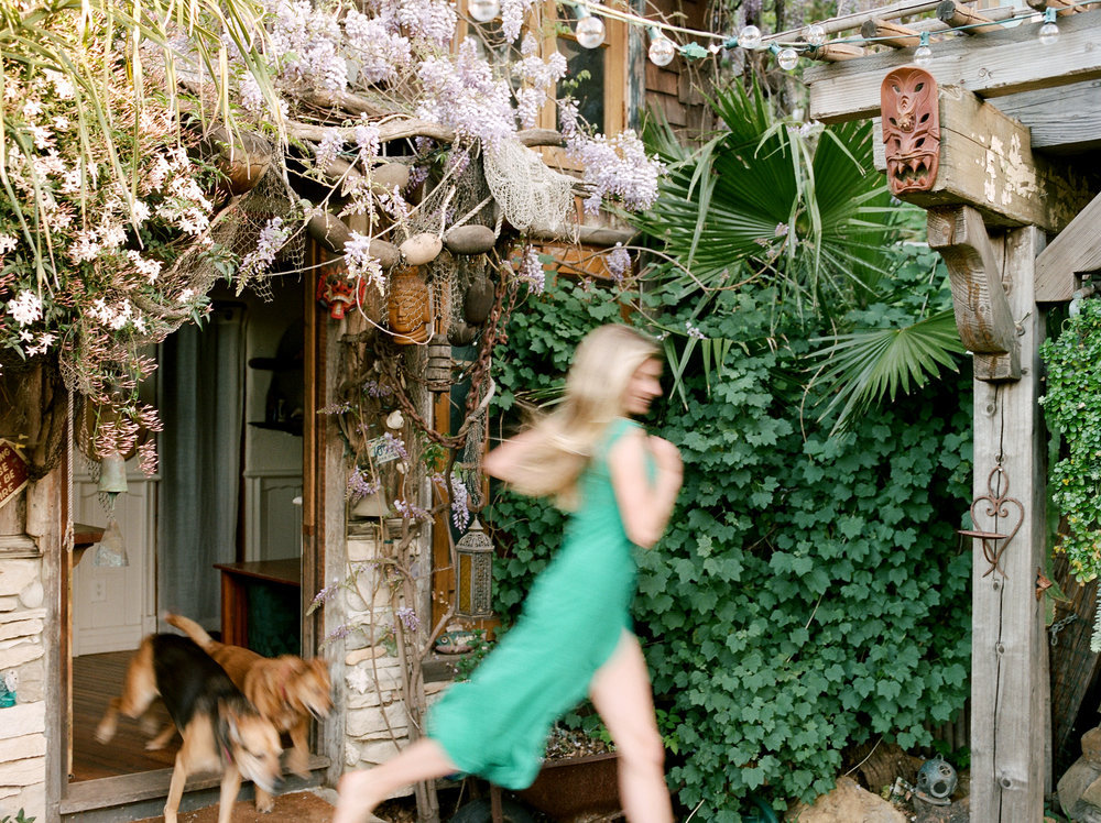 A woman in a green dress running with a dog in front of a house.
