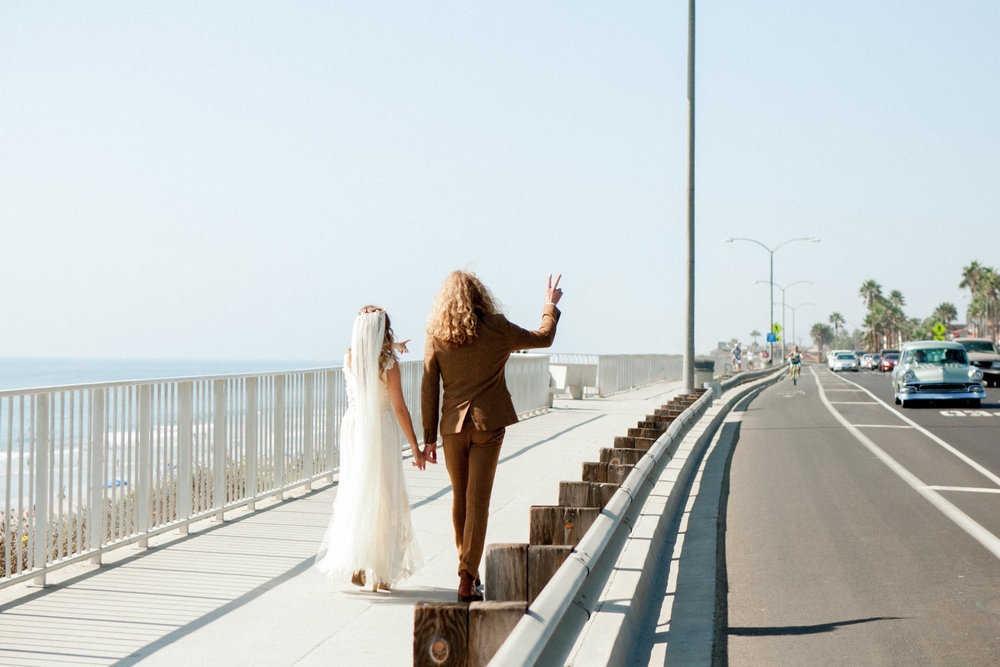 A bride and groom walking on a bridge near the ocean.
