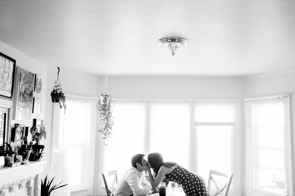 A couple kissing at a table in a living room.