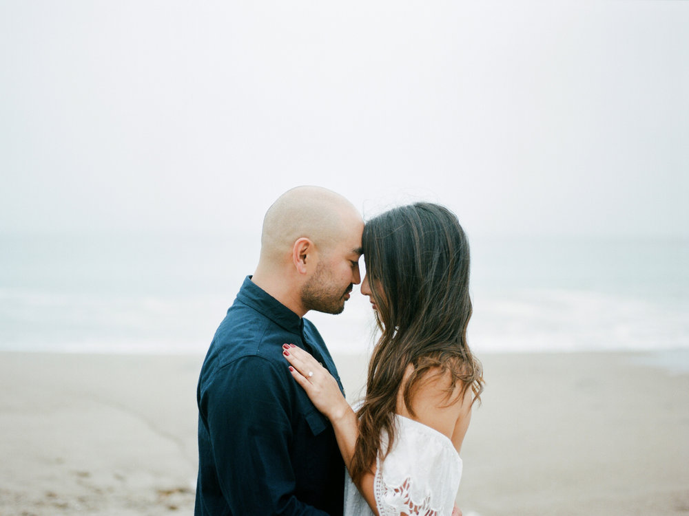 A couple embraces on the beach during their engagement session.