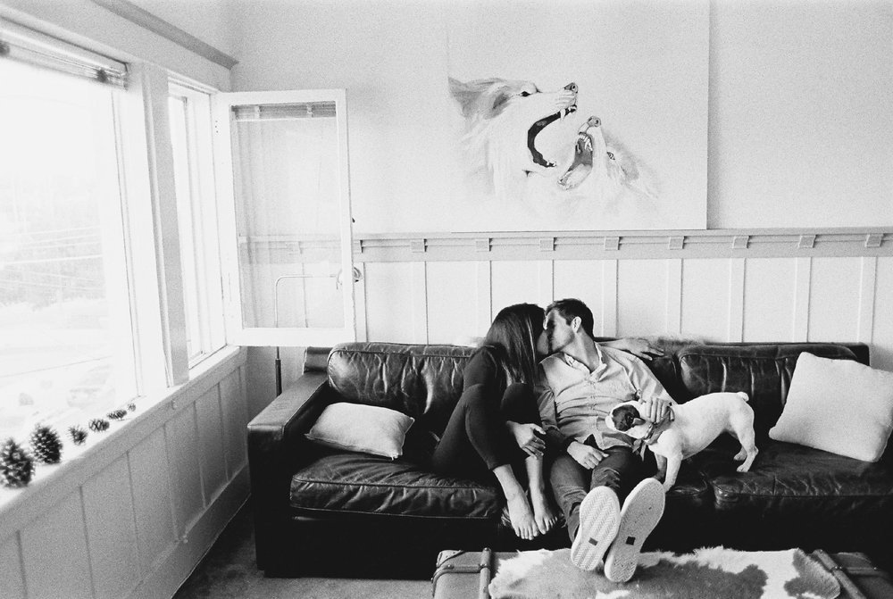 A black and white photo of a couple sitting on a couch with a dog.