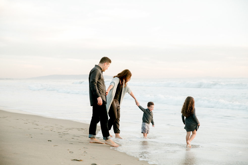 mother, father, and two chuldren walk on the beach in the surf at sunset