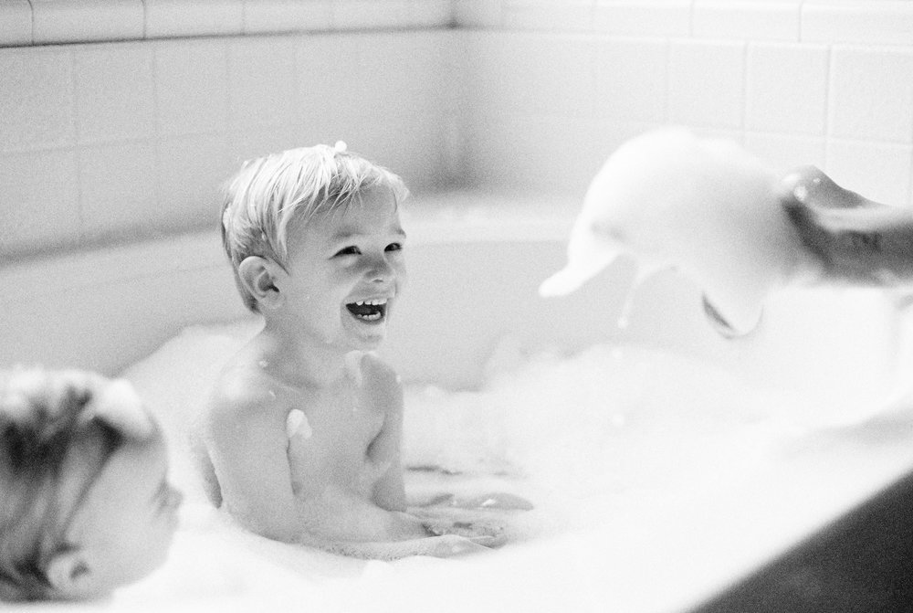 kids in a bubble bath laughing at mom holding bubbles