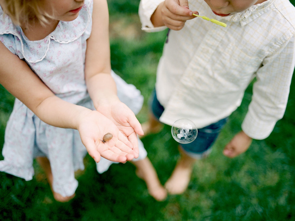 close up of two young children holding a snail and blowing bubbles