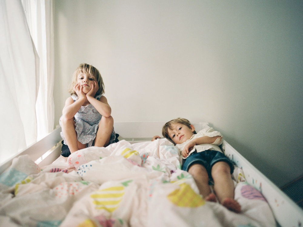 boy and girl twins sitting in bed looking at the camera straight faced