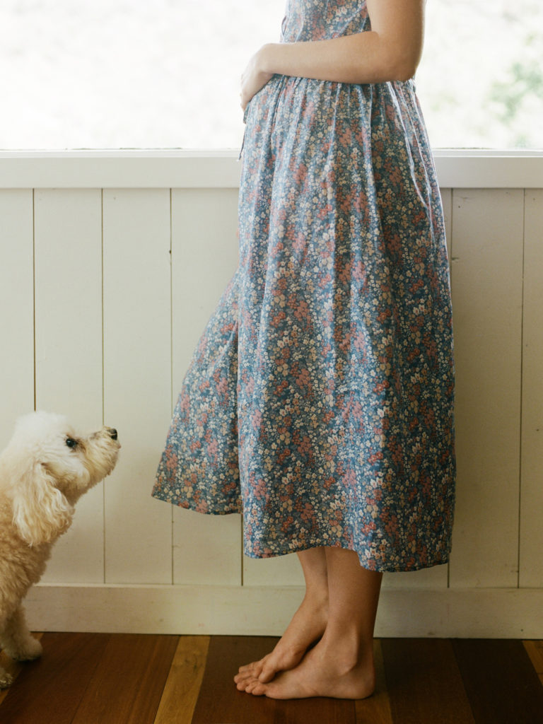 pregnant woman in vintage dress holding belly white white fluffy dog looks up at her