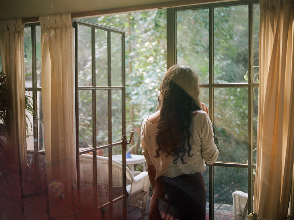 woman looking out a glass window into nature