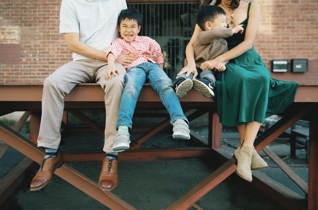 family of four sitting on a metal dock with parents tickling the children while they laugh