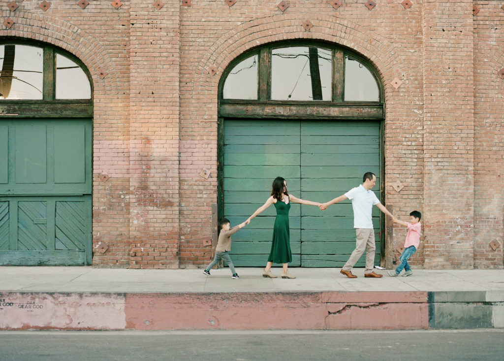 family of four holding hands in a row with brick building in background