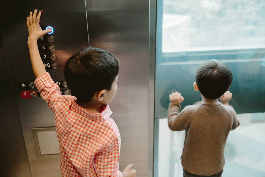 young boys riding in an elevator and pushing buttons