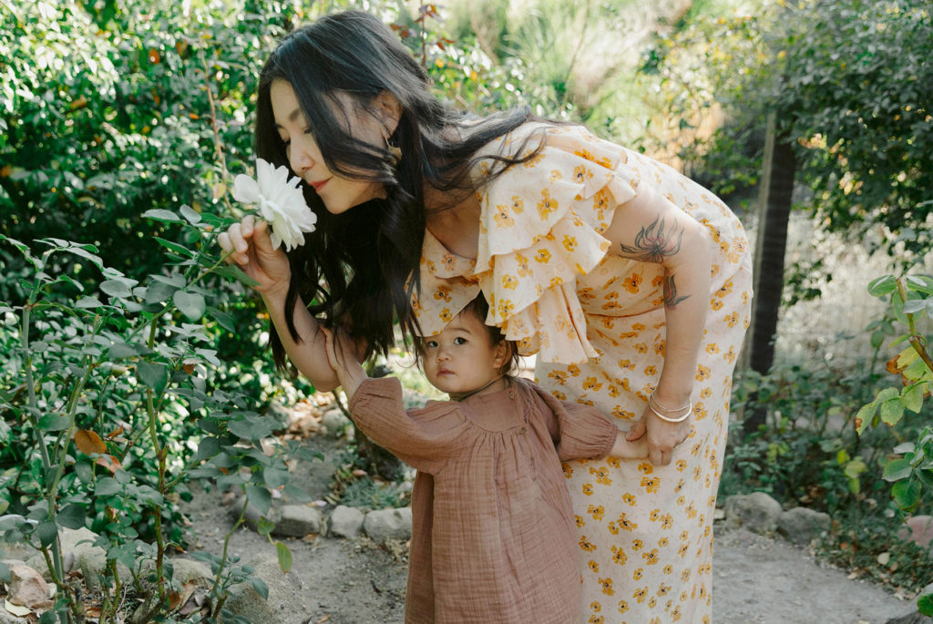 A woman in a yellow dress embraces a flower in her hand during a family photography session.