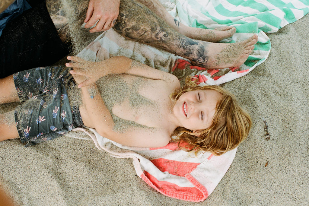 A child is lounging on a towel in the sand during a family photography session.