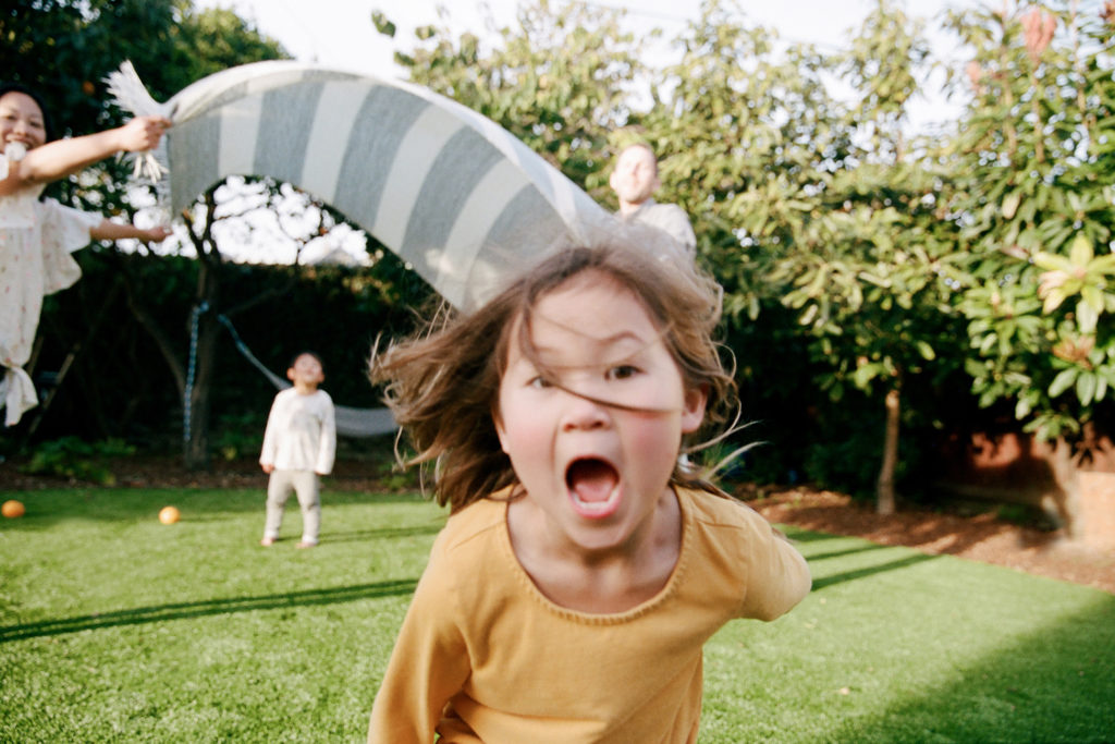 A girl is enjoying family photography as she runs around with a kite in her backyard.