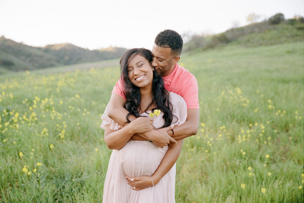 A family captured in a field of yellow flowers during a maternity photoshoot.