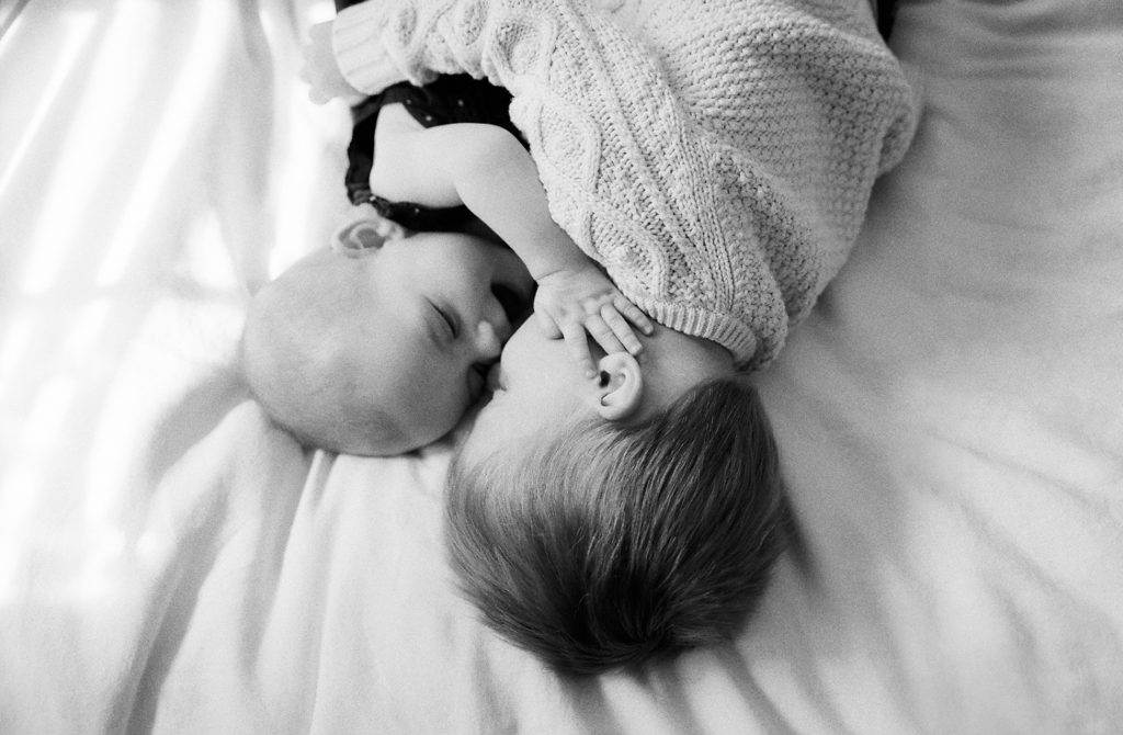 Black and white family photography of two babies laying on a bed.