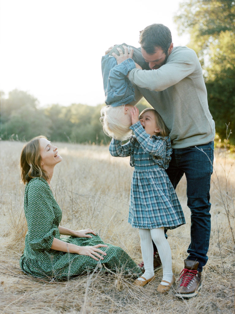 A family is captured in a field during a joyful session of family photography.
