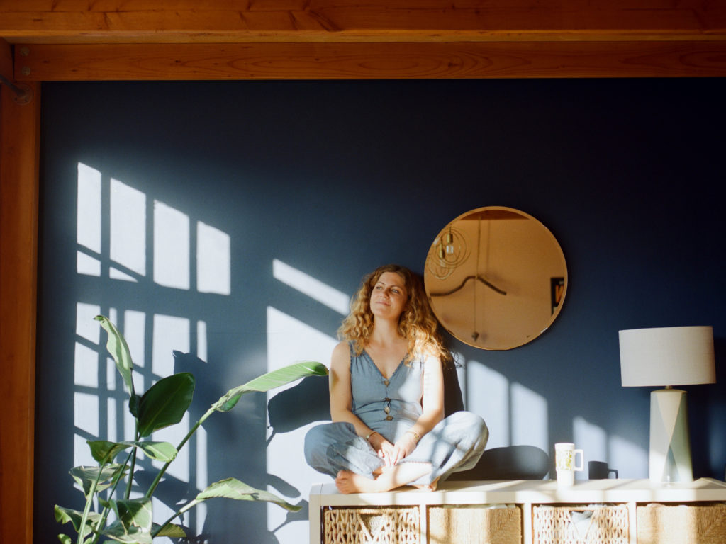 A woman sitting in a room with blue walls and a plant.