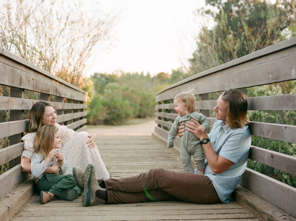 Family sitting on a wooden bridge captured in a family photography session.