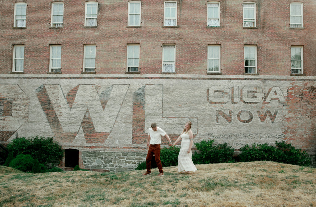 A bride and groom standing in front of a brick building with the words owl now.