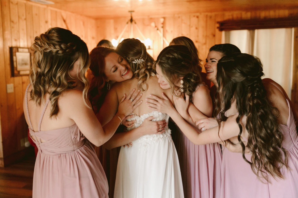 A bride and her bridesmaids hugging in a cabin.