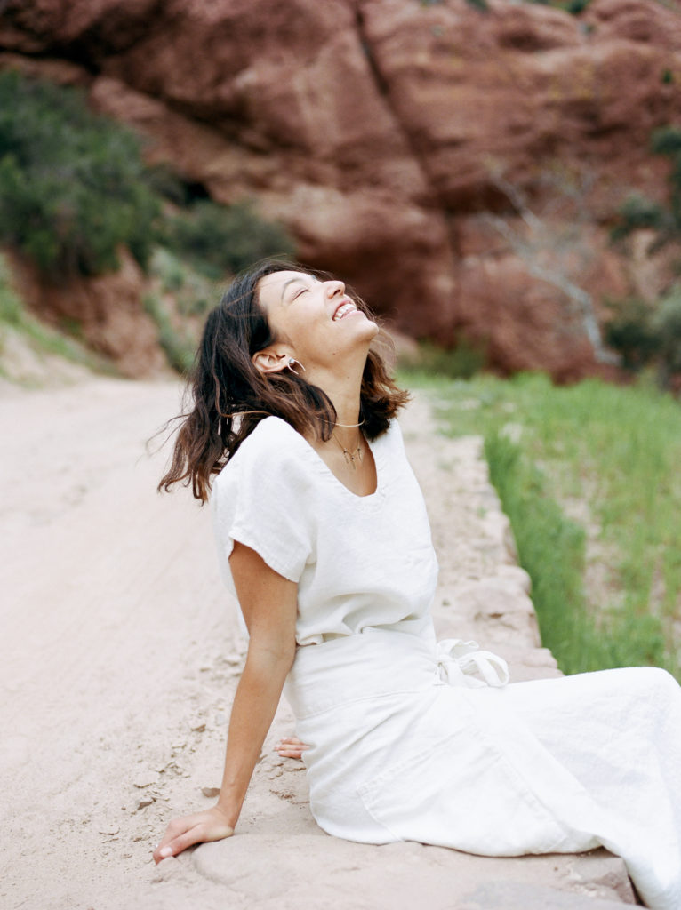 A woman in a white dress sitting on a dirt road.