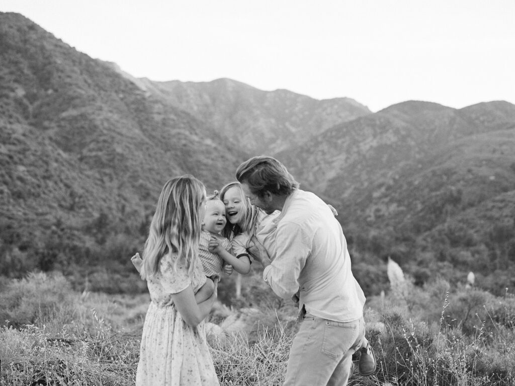 black and white film photograph of family playfully hugging with mountains in the background