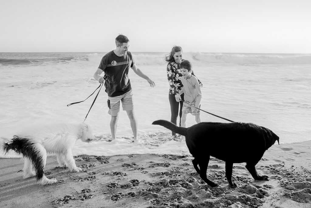 A black and white photo of a family walking their dog on the beach.