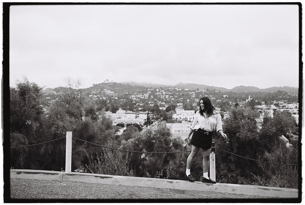 A black and white photo of a woman standing on a fence.