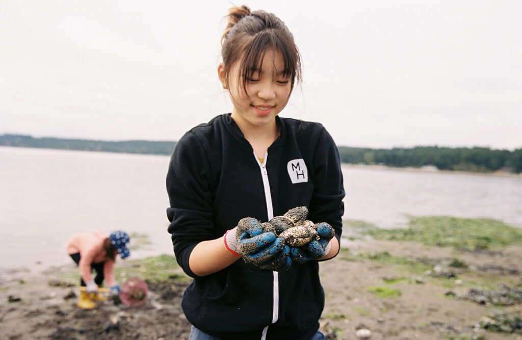 A girl holding a bucket of shells on a beach.
