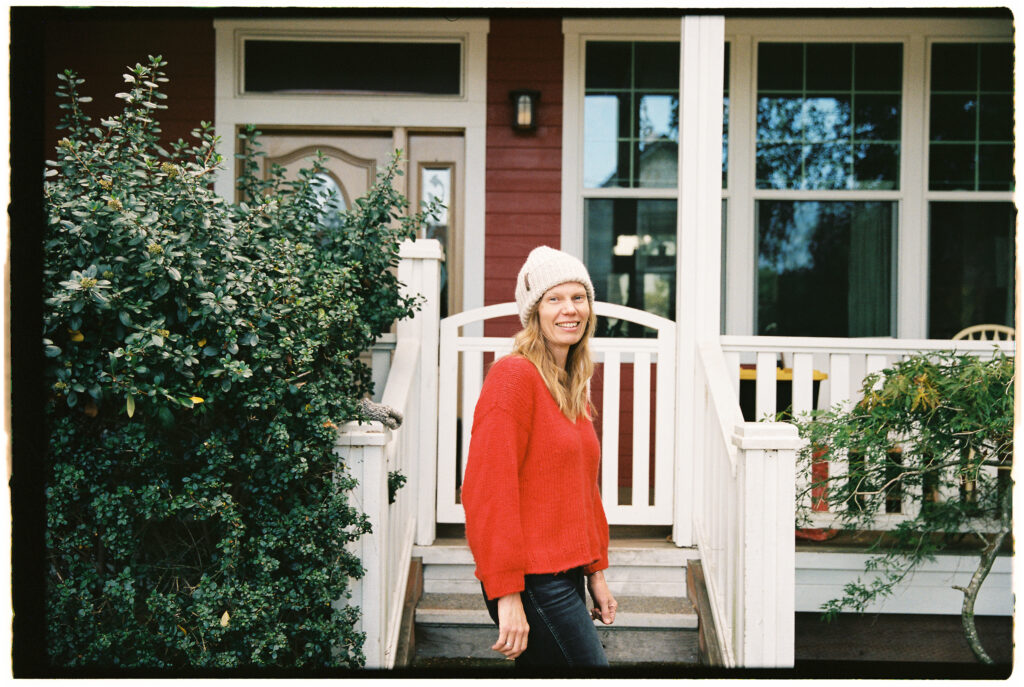 A woman in a red sweater standing on the steps of a house.