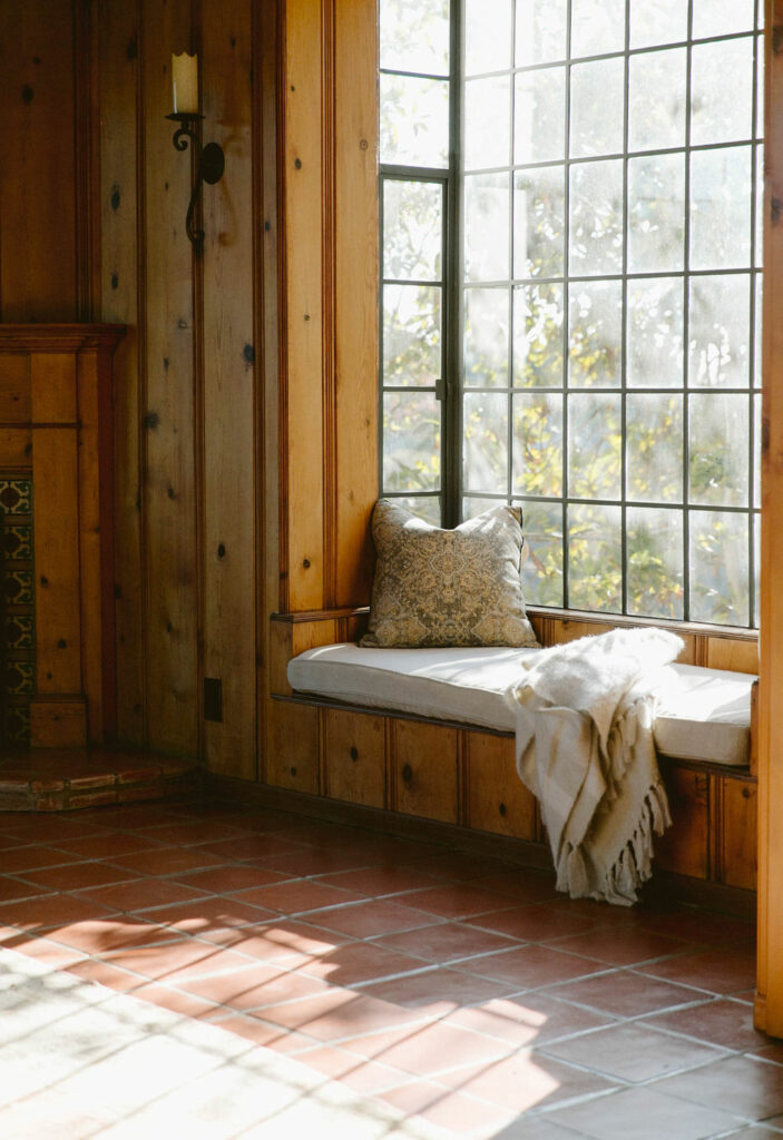 Cozy window nook with cushion, pillow, and a throw blanket, bathed in natural sunlight.