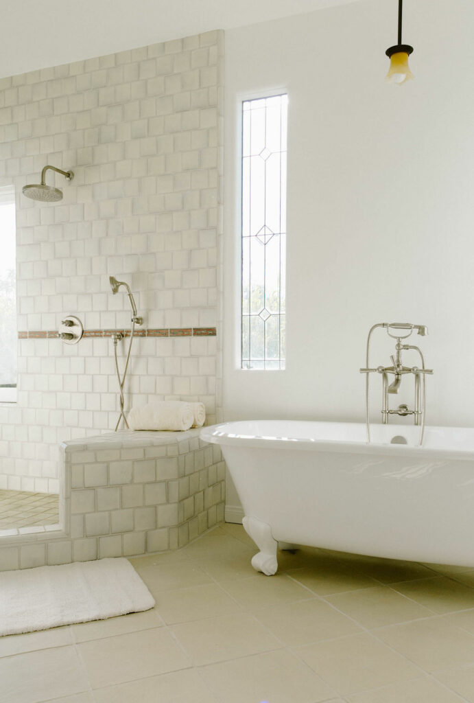 A light-filled bathroom with a classic claw-foot tub, white subway tiles, and a narrow window.