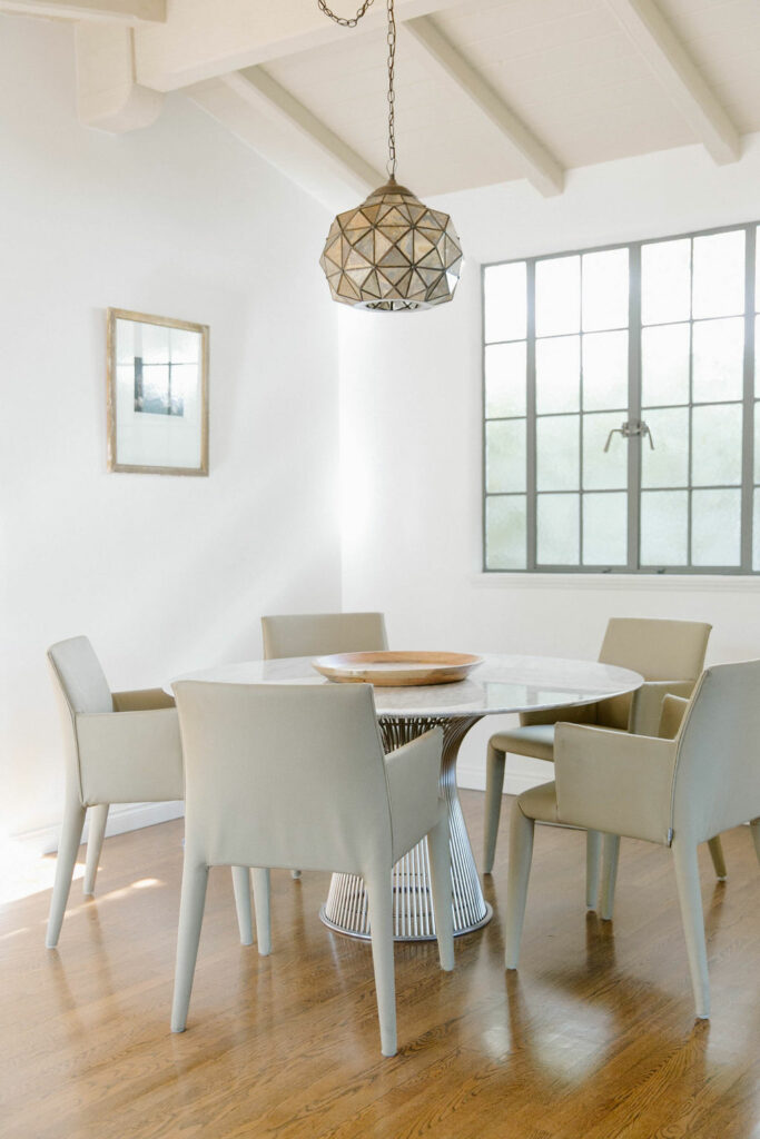 A minimalist dining room with a modern geometric pendant light, a round table, and light-toned chairs.