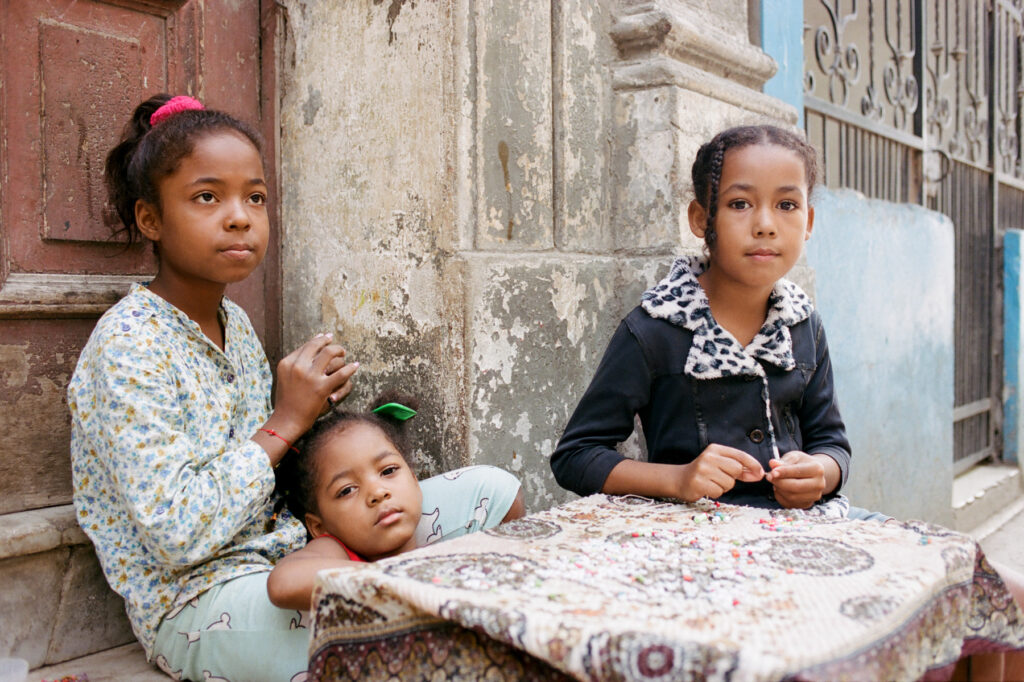 Two young girls sitting on a step with a toddler, in a quaint urban alleyway.