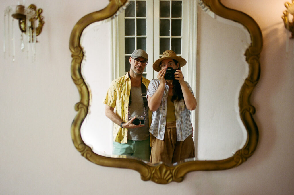Two people taking a mirror selfie in a warmly lit room.