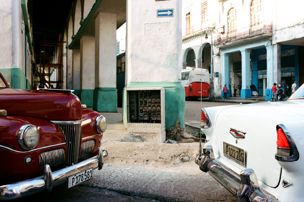 Vintage cars parked on a street in a cuban city with colorful buildings and urban decay visible in the background.