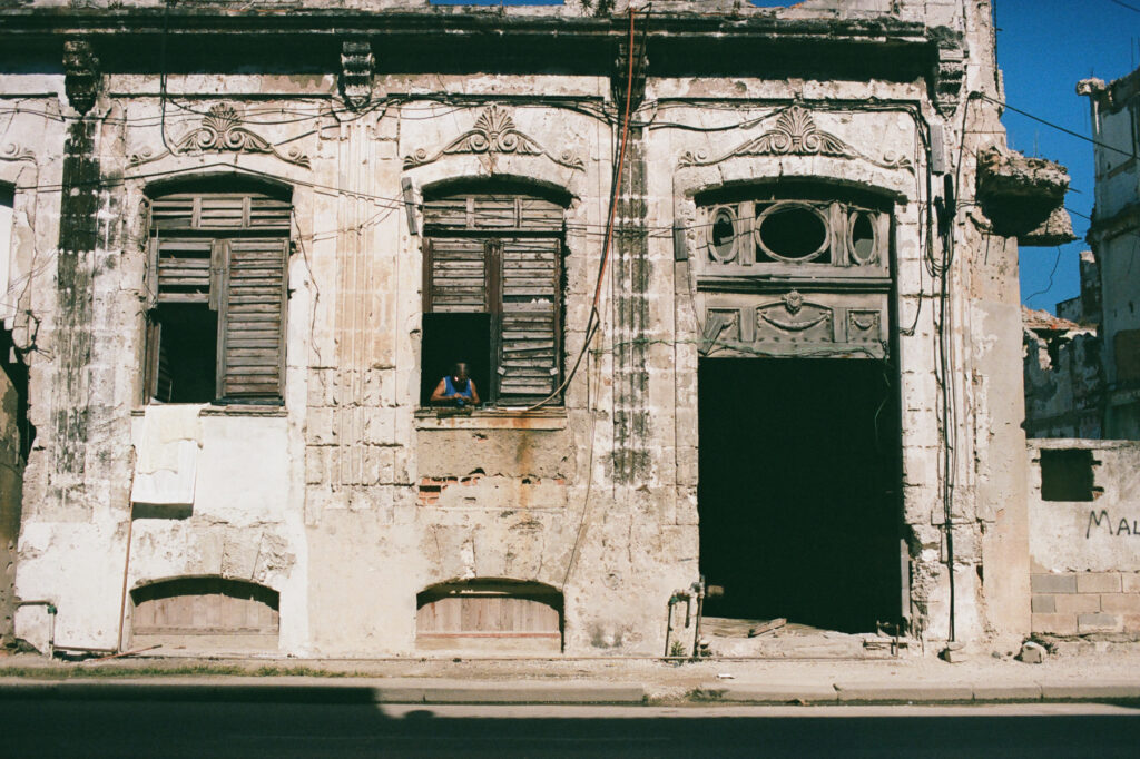 Dilapidated building with a person sitting in a window opening.