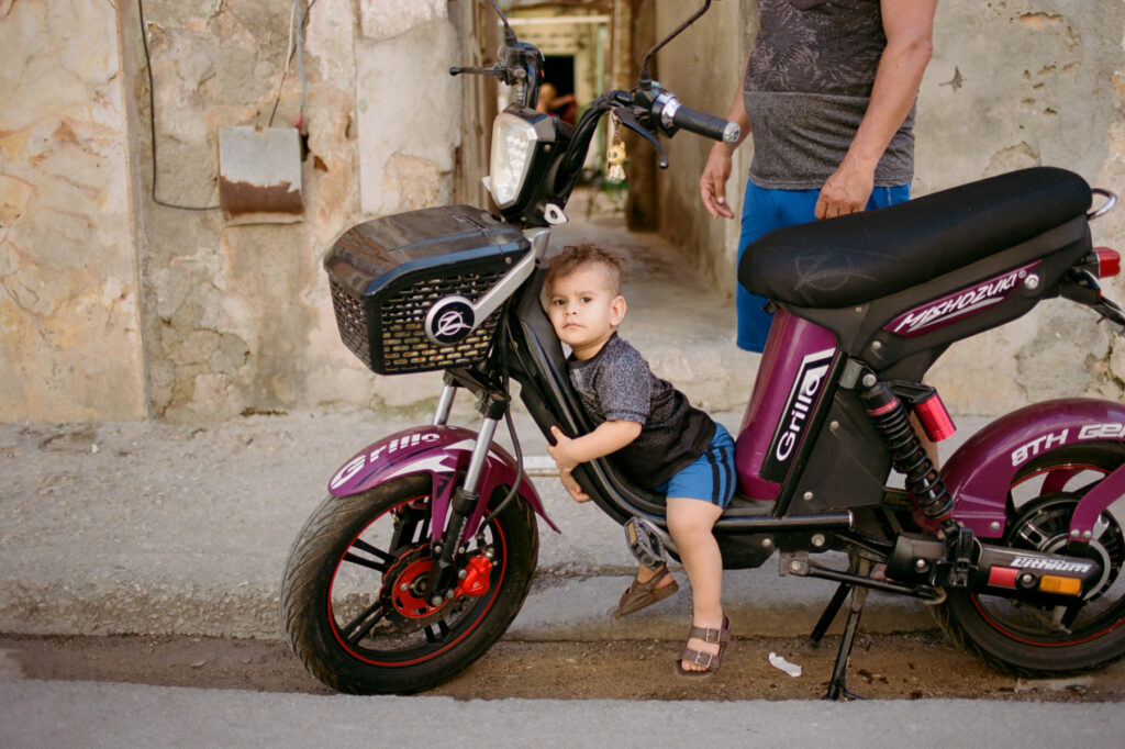 A young child leaning on a parked moped in a narrow street.