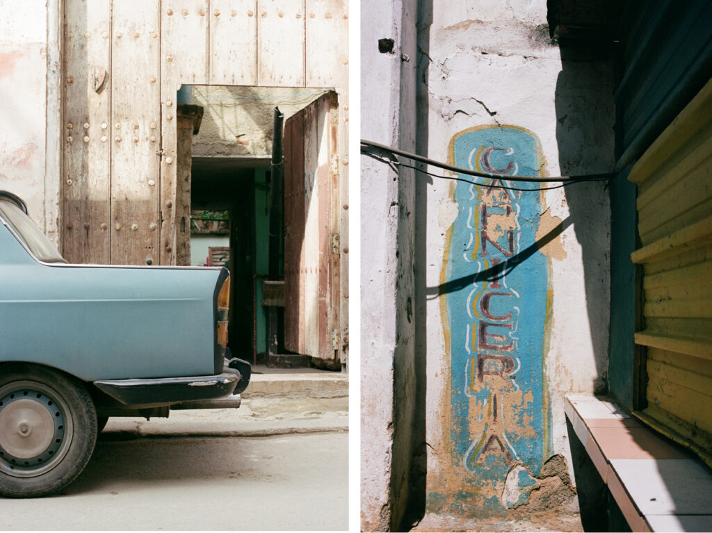 Vintage blue car parked beside a rustic building with weathered walls and a faded "cantería" sign.