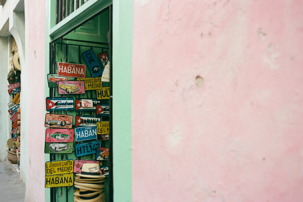 An array of cuban license plates and souvenirs displayed beside a pastel-colored doorway.