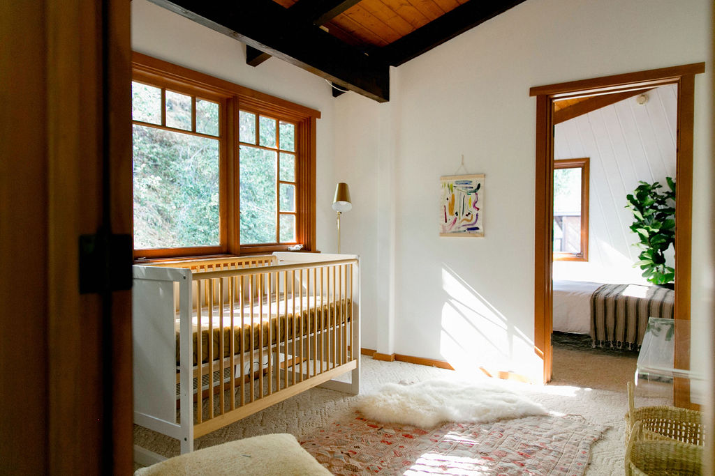 A bright and airy nursery room with a crib, white walls, and natural light streaming in through the windows.