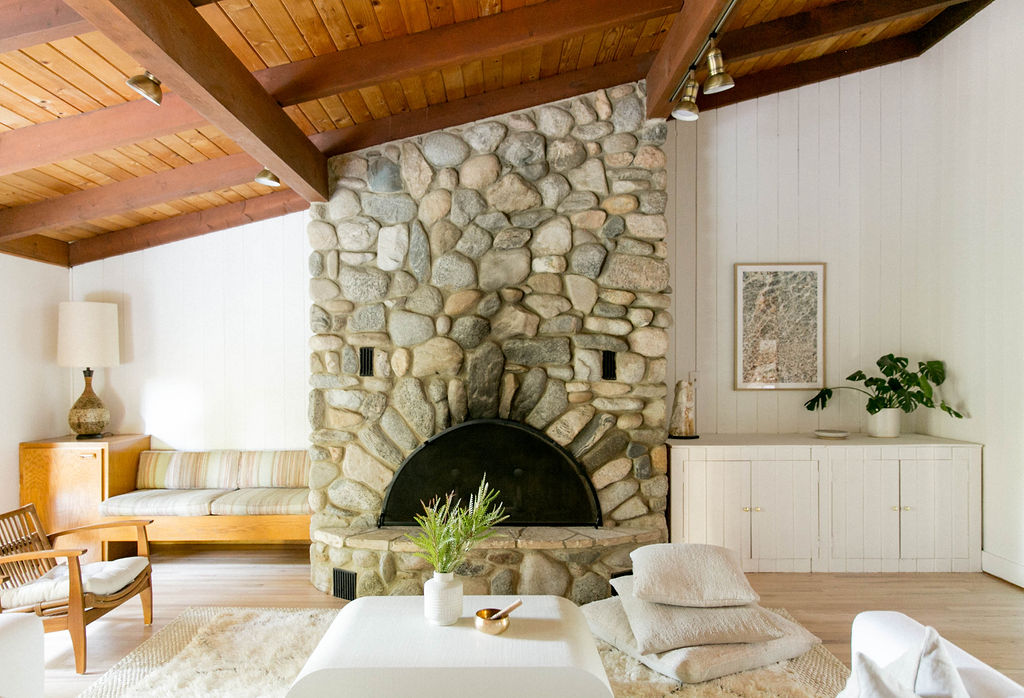 A cozy living room featuring a large stone fireplace, wooden beams, and modern furnishings.