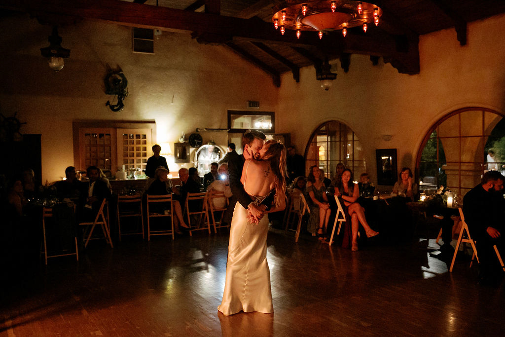A couple sharing a dance in a dimly lit room with onlooking guests.